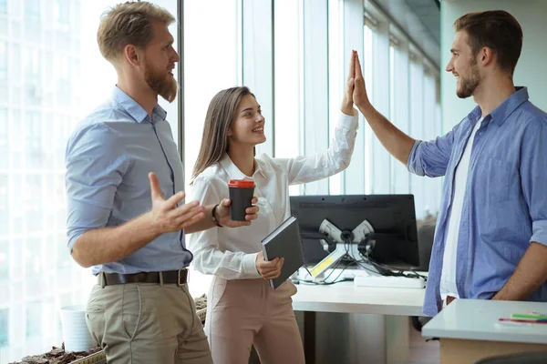 Happy young people standing in office and giving high five to their colleagues.