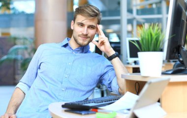 Oturma ve ofiste çalışırken bilgisayar monitörü arayan genç adam.