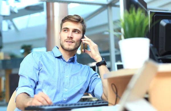 Hombre de negocios sonriente sentado y usando el teléfono móvil en la oficina . —  Fotos de Stock