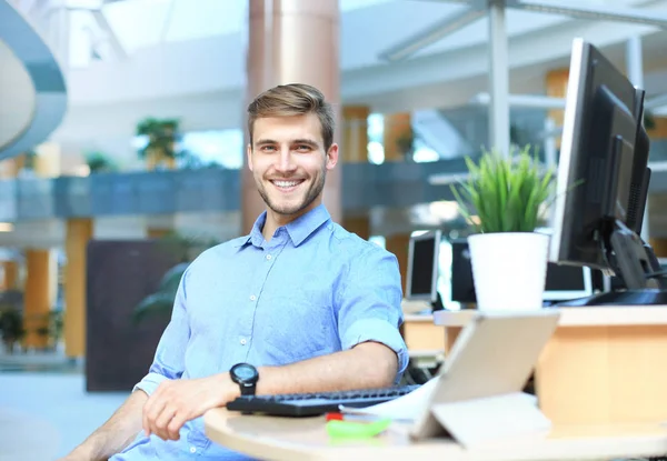 Retrato del hombre feliz sentado en el escritorio de la oficina, mirando a la cámara, sonriendo . — Foto de Stock