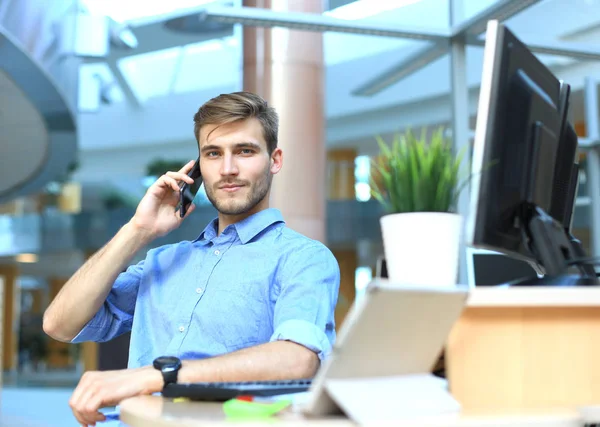 Hombre de negocios sonriente sentado y usando el teléfono móvil en la oficina . — Foto de Stock