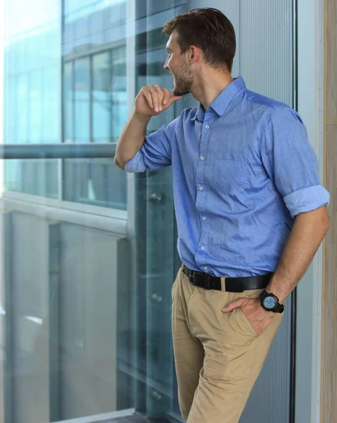 Joven de pie cerca de la ventana en su oficina mientras piensa en sus objetivos . — Foto de Stock