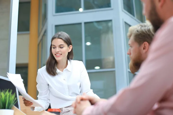 Grupo de jóvenes en ropa casual sentados en el escritorio de la oficina y discutiendo algo mientras miran PC juntos . — Foto de Stock