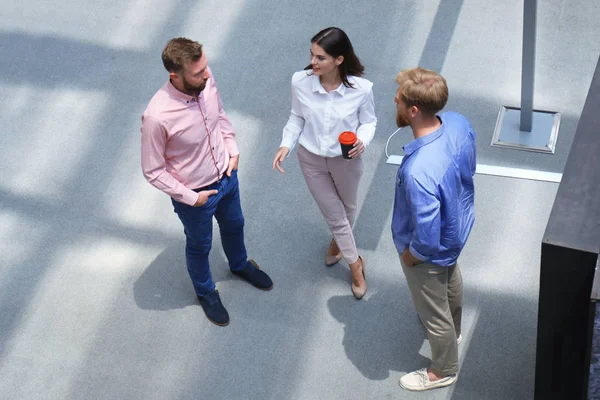 Vue du dessus des jeunes gens modernes en vêtements décontractés intelligents discutant affaires tout en se tenant dans le bureau créatif . — Photo