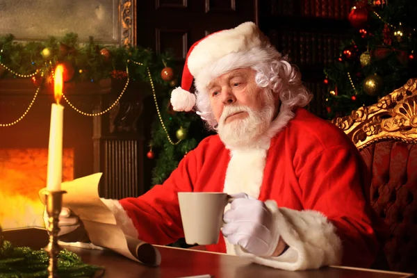 Retrato de Papai Noel feliz sentado em seu quarto em casa perto da árvore de Natal e lendo carta de Natal ou lista de desejos. — Fotografia de Stock