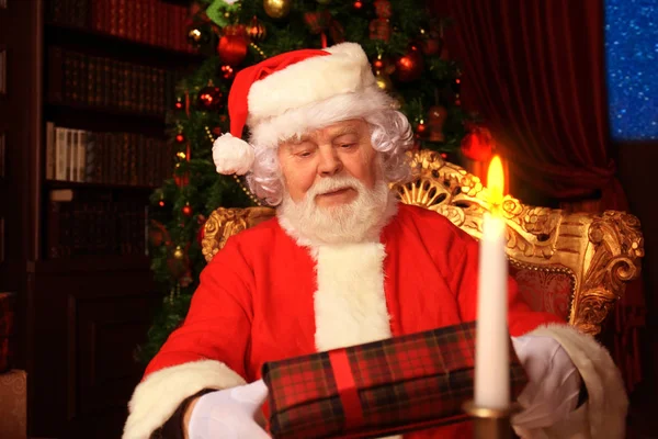 Retrato de Papai Noel feliz sentado em seu quarto em casa perto da árvore de Natal com caixa de presente. — Fotografia de Stock