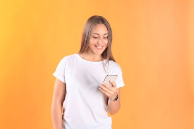 Cep telefonunuzun temel giyim sarı arka plan üzerinde izole giymiş genç kadın.