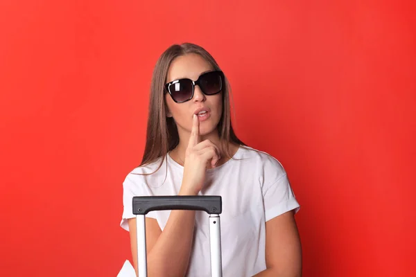 Jeune fille touristique en vêtements décontractés d'été, avec des lunettes de soleil, valise rouge, isolé sur fond rouge . — Photo