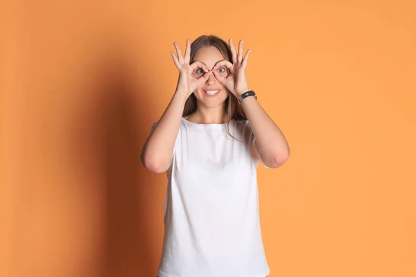 Νεαρή γυναίκα σε βασικά είδη ένδυσης χαμογελώντας βλέπουν κάμερα μέσα από τρύπες που γίνονται με τα δάχτυλα που απομονώνονται σε κίτρινο φόντο. — Φωτογραφία Αρχείου