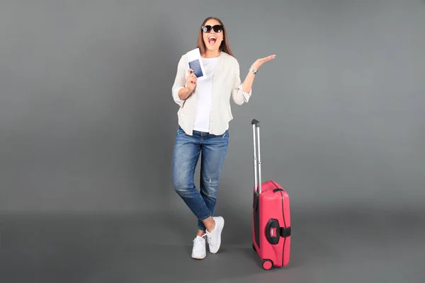 Joven turista en ropa casual de verano, con gafas de sol, maleta roja, pasaporte, entradas de fondo gris aislado . — Foto de Stock