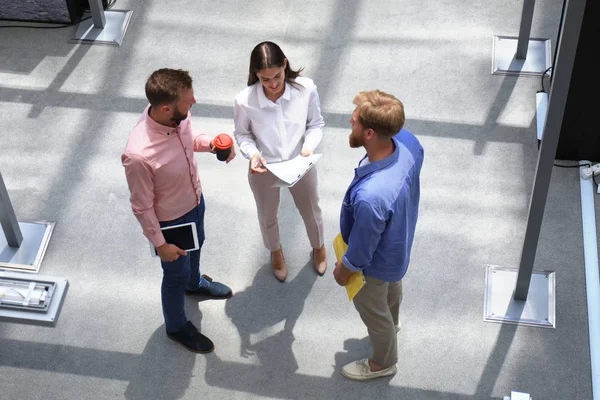 Vue du dessus des jeunes gens modernes en vêtements décontractés intelligents discutant affaires tout en se tenant dans le bureau créatif . — Photo