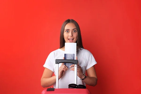 Jeune fille touristique en vêtements décontractés d'été, avec des lunettes de soleil, valise rouge, passeport isolé sur fond rouge . — Photo