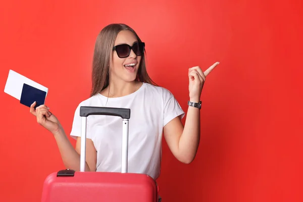 Jeune fille touristique en vêtements décontractés d'été, avec des lunettes de soleil, valise rouge, passeport isolé sur fond rouge . — Photo