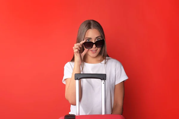 Jeune fille touristique en vêtements décontractés d'été, avec des lunettes de soleil, valise rouge, isolé sur fond rouge . — Photo