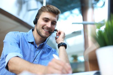 Gülümseyen yakışıklı genç erkek çağrı merkezi operatörü.