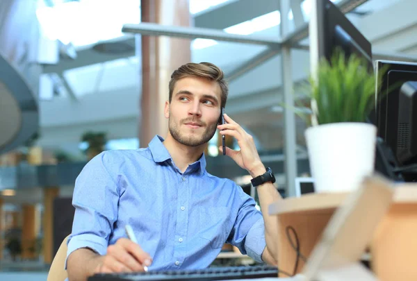 Empresário sorridente sentado e usando telefone celular no escritório . — Fotografia de Stock