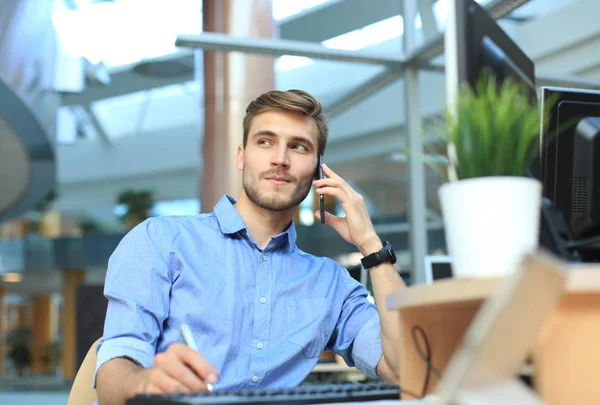 Uomo d'affari sorridente seduto e utilizzando il telefono cellulare in ufficio . — Foto Stock