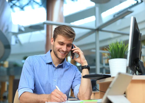 Hombre de negocios sonriente sentado y usando el teléfono móvil en la oficina . — Foto de Stock