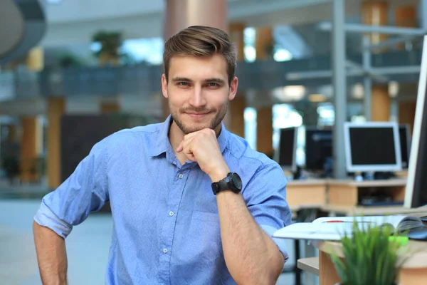 Retrato de homem feliz sentado na mesa do escritório, olhando para a câmera, sorrindo . — Fotografia de Stock