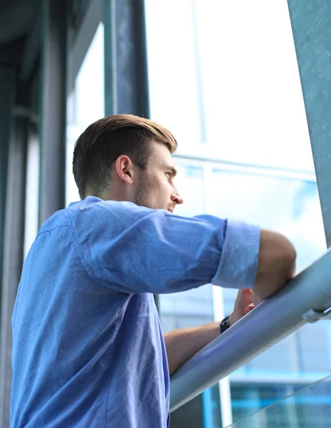 Joven de pie cerca de la ventana en su oficina mientras piensa en sus objetivos . —  Fotos de Stock