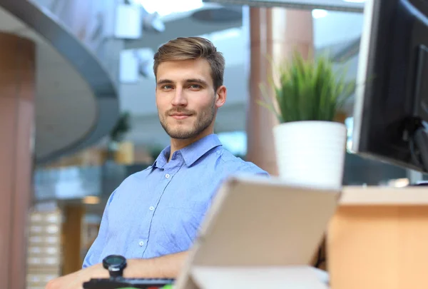 Portrait of happy man sitting at office desk, looking at camera, smiling.