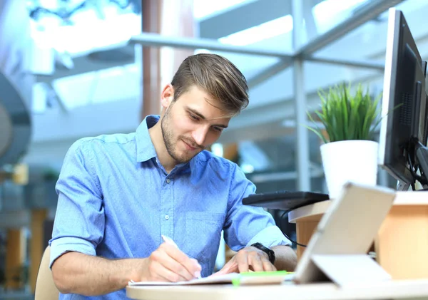 Porträtt av stilig leende man i ledig skjorta med anteckningar på arbetsplatsen. — Stockfoto