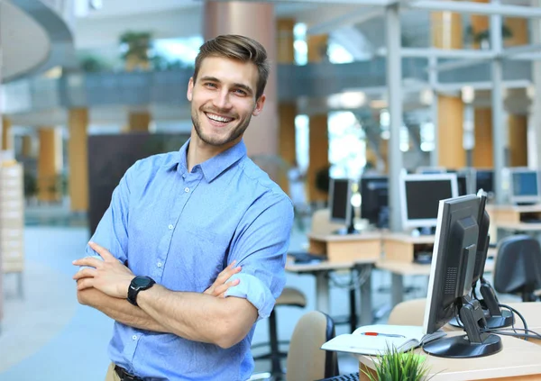 Junger Mann posiert selbstbewusst und positiv in professionellem Büro mit Platz am Arbeitsplatz. — Stockfoto