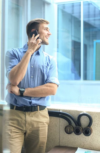 Χαμογελώντας επιχειρηματίας στέκεται και η χρήση του κινητού τηλεφώνου στο γραφείο. — Φωτογραφία Αρχείου