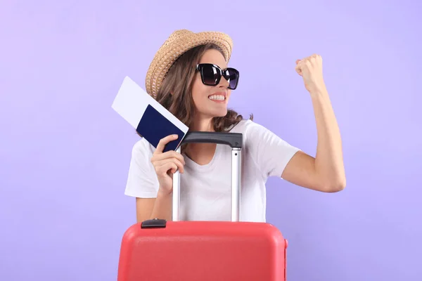 Jonge toeristische meisje in zomer casual kleding, met paspoort geïsoleerd op een paarse achtergrond, zonnebril, rood koffer. — Stockfoto