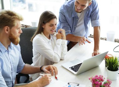 Grup içinde smart casual modern gençlerin giyim laptop işaret ve ofiste otururken gülümseyen