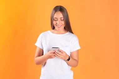 Cep telefonunuzun temel giyim sarı arka plan üzerinde izole giymiş genç kadın.