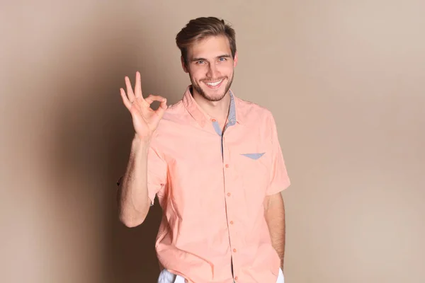 Smiling young man standing isolated over beige background, showing ok gesture. — Stock Photo, Image