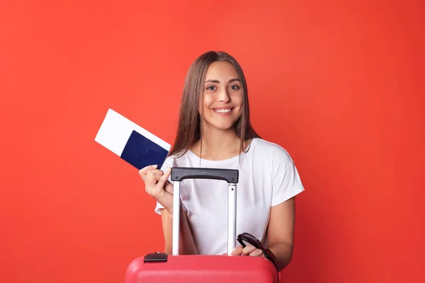 Jeune fille touristique en vêtements décontractés d'été, avec des lunettes de soleil, valise rouge, passeport isolé sur fond rouge . — Photo