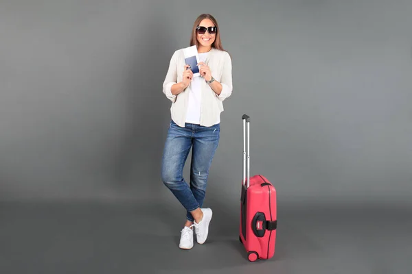 Joven turista en ropa casual de verano, con gafas de sol, maleta roja, pasaporte, entradas de fondo gris aislado . — Foto de Stock