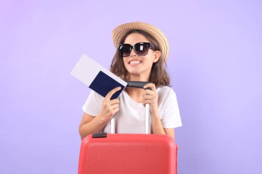 Güneş gözlüğü, kırmızı çanta, mor arka plan üzerinde izole pasaport ile yaz casual giysili genç turist kızı.
