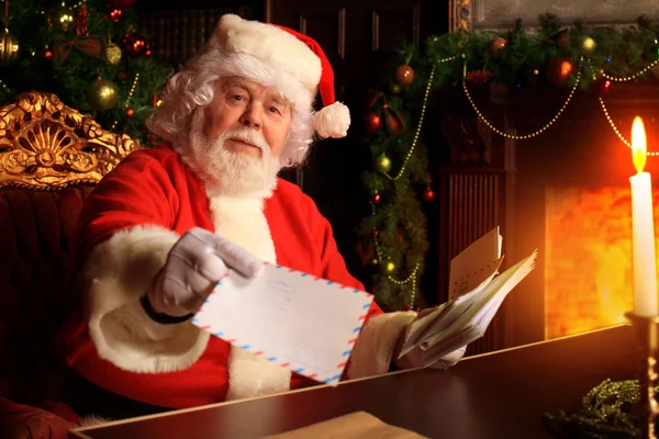 Papai Noel sentado na árvore de Natal, segurando cartas de Natal e tendo um descanso junto à lareira. — Fotografia de Stock