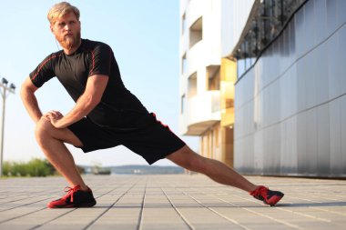 Açık havada duran süre çalıştırmadan önce germe yapan yakışıklı genç erkek egzersizleri.