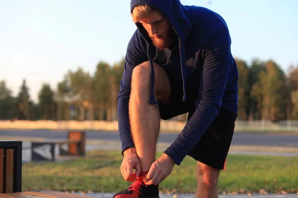 Atleta en forma. Guapo hombre adulto corredor atando cordones al atardecer o al amanecer . — Foto de Stock