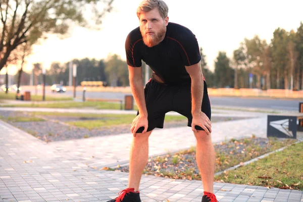 Handsome young man after run resting after jog in the city at sunset or sunrise.