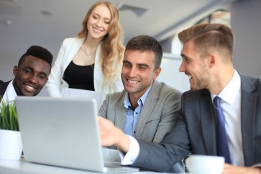 Girişim ekibi, modern parlak ofis içinde toplantı ve dizüstü bilgisayar üzerine çalışıyor.