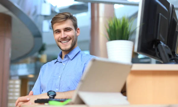 Porträtt av lycklig man sitter vid skrivbord, tittar på kameran, leende. — Stockfoto