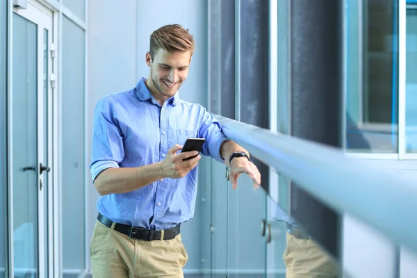 Mosolygó üzletember, állandó, és a mobiltelefon használata az office. — Stock Fotó