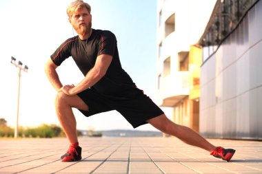 Açık havada duran süre çalıştırmadan önce germe yapan yakışıklı genç erkek egzersizleri.