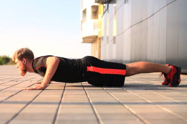 Spor elbiseli yakışıklı genç adam dışarıda egzersiz yaparken kalas pozisyonunu koruyor..