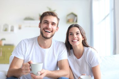 Evdeki kanepede oturup televizyon seyreden ve gülen genç çift..