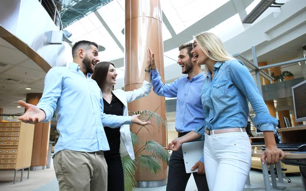 Glada unga människor står i office och ger hög fem till sina kollegor. — Stockfoto