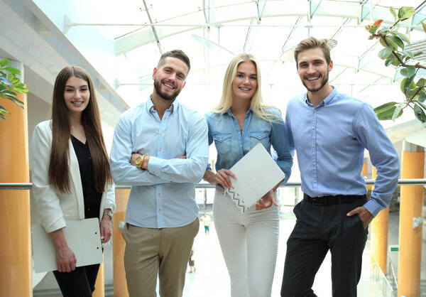 Young modern colleagues in smart casual wear looking at camera standing in the creative office