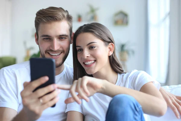 Pareja joven tomando una selfie en el sofá en casa en la sala de estar . —  Fotos de Stock