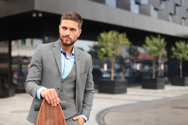 Selbstbewusster junger Geschäftsmann, der mit Longboard auf die Straße geht. — Stockfoto