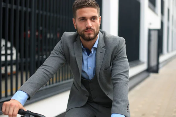 Guapo joven hombre de negocios montar en bicicleta al aire libre en la ciudad . — Foto de Stock